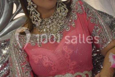 Deux femmes en robes traditionnelles violettes ornées de bijoux, posant devant un fond clair avec un fauteuil argenté.