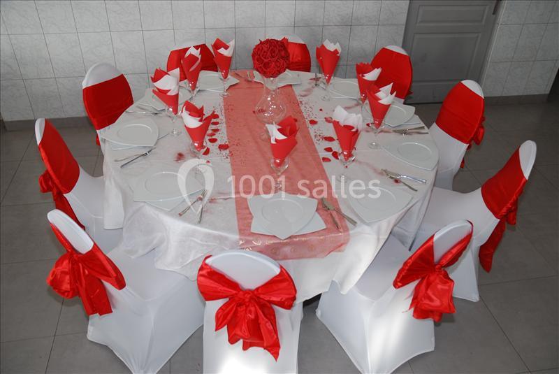 Table ronde décorée pour un événement, nappes blanches, serviettes et rubans rouges, centre de table floral rouge.