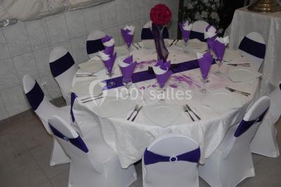 Deux femmes en robes traditionnelles violettes ornées de bijoux, posant devant un fond clair avec un fauteuil argenté.