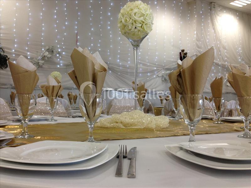 Table élégamment dressée avec nappes blanches, serviettes pliées, verres et centre de table floral dans une salle décorée.