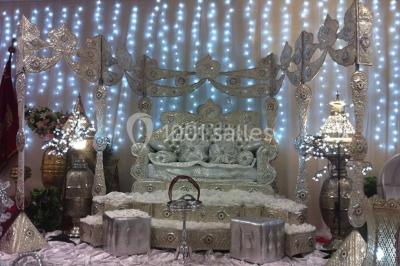 Deux femmes en robes traditionnelles violettes ornées de bijoux, posant devant un fond clair avec un fauteuil argenté.