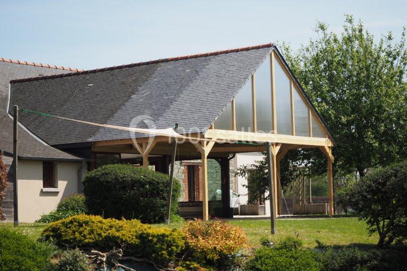 Abri en bois avec toit en ardoise et paroi vitrée, situé dans un jardin verdoyant.