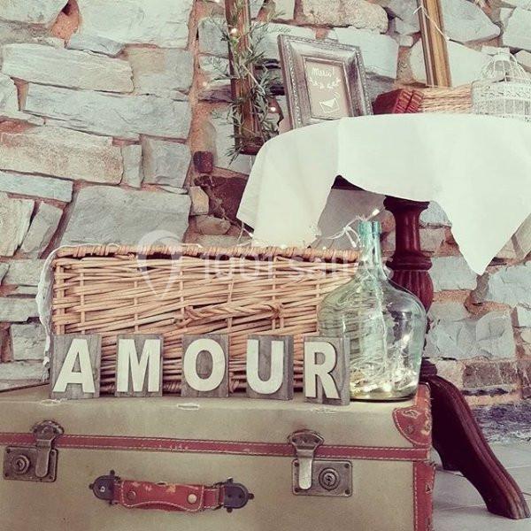 Décoration vintage avec une valise ancienne, des lettres formant ’AMOUR’, un panier en osier et une carafe en verre.
