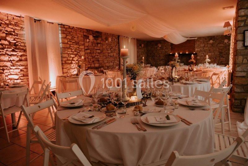 Salle de réception décorée avec des tables rondes dressées, chaises blanches et éclairage chaleureux.