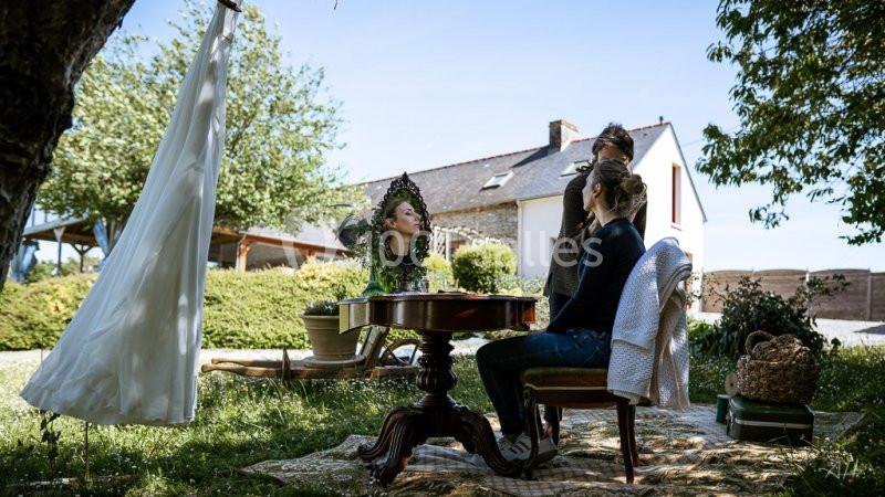 Deux femmes assises dans un jardin, l'une se faisant coiffer devant un miroir, robe suspendue à un arbre.