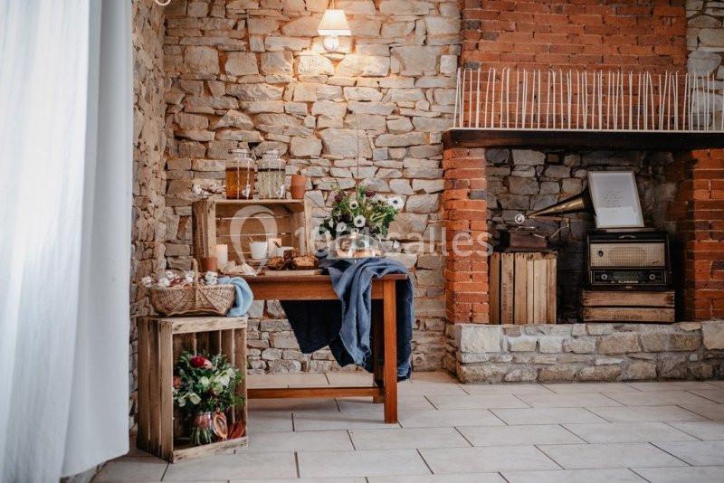 Table en bois décorée avec des fleurs, des boissons et des aliments, dans une pièce au mur en pierre et cheminée en briques.