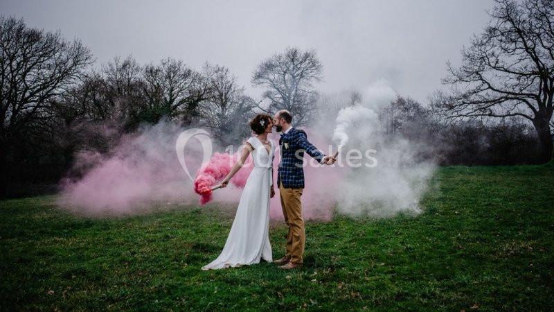Un couple dans un champ tient des fumigènes roses et blancs, entouré de brouillard coloré.