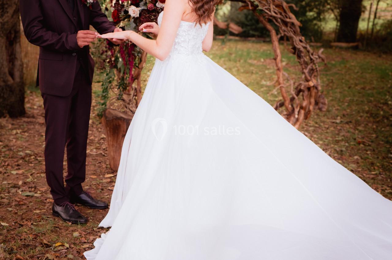 Un couple échange des alliances lors d'une cérémonie de mariage en plein air, entouré de végétation et d'une arche florale.