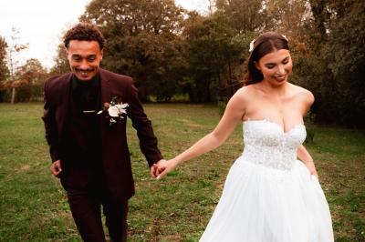 Un couple en tenue de mariage se regarde sous une pergola illuminée de guirlandes lumineuses.