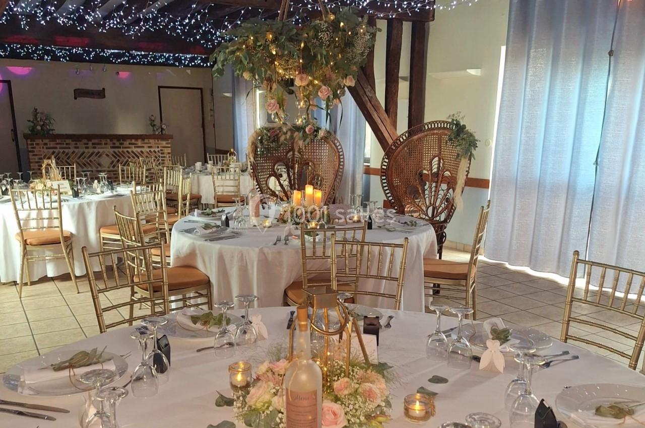 Salle de réception décorée avec des tables rondes, des chaises dorées, des guirlandes lumineuses et des fleurs.
