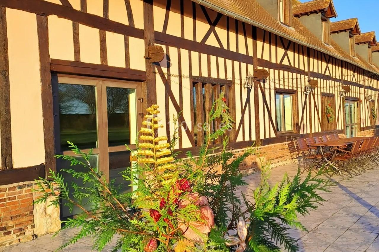 Façade d'une maison à colombages avec toit en pente, terrasse pavée et composition florale au premier plan.