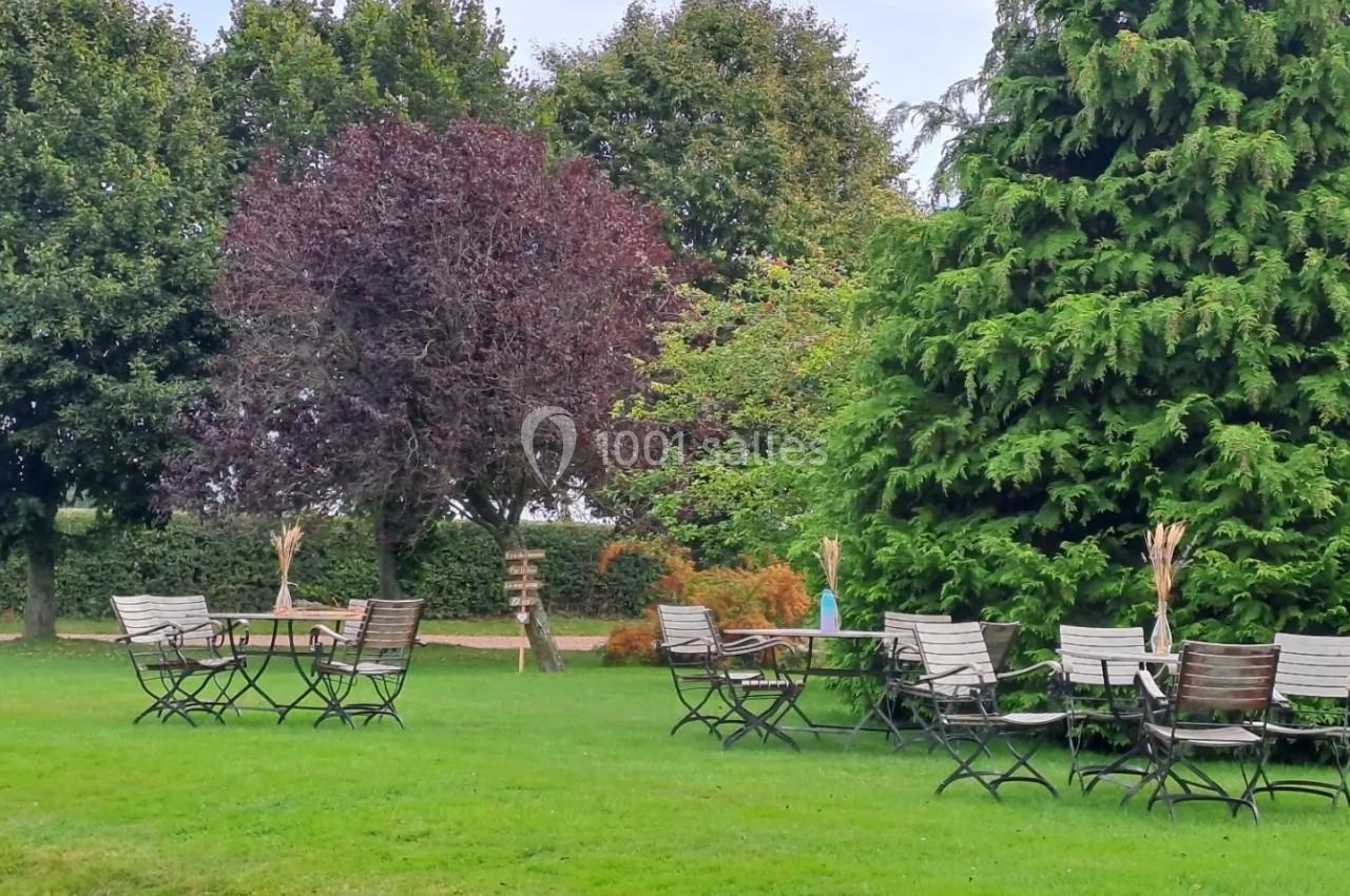 Chaises et tables en métal disposées sur une pelouse verte, entourées d'arbres dans un cadre extérieur paisible.
