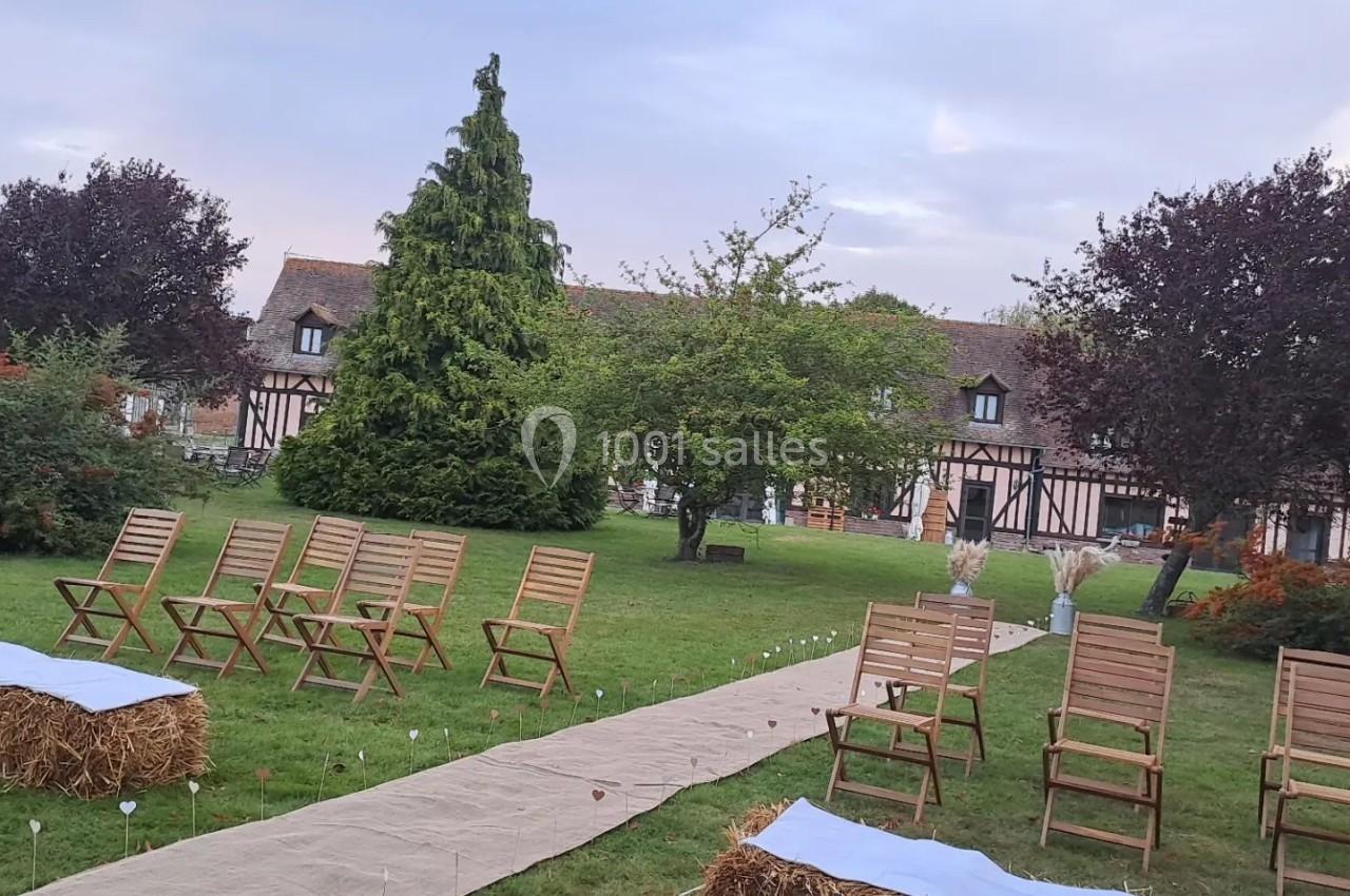 Allée centrale en tissu bordée de chaises en bois et bottes de paille, dans un jardin verdoyant devant une maison à…