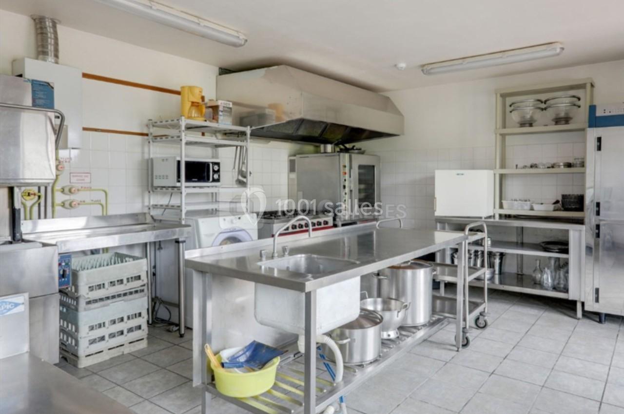 Cuisine professionnelle équipée avec plans de travail en inox, étagères de rangement, évier et appareils électroménagers.