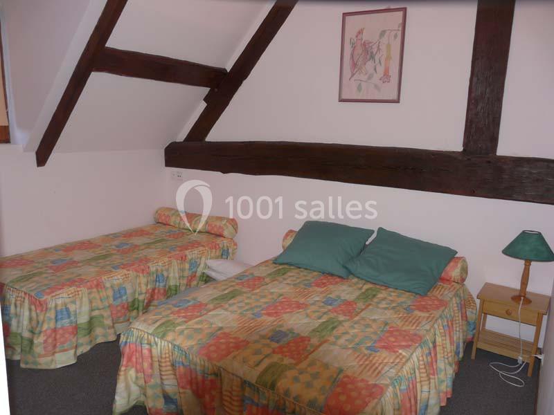 Deux lits simples avec couvre-lits colorés dans une chambre mansardée, décorée de poutres apparentes et d'une lampe de…