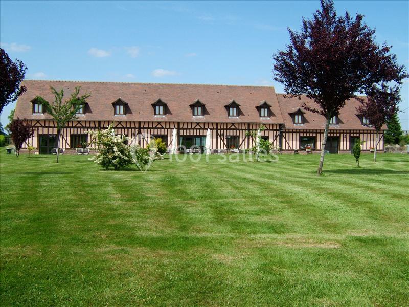 Bâtiment à colombages avec toit en pente, entouré d'une pelouse verte et d'arbres sous un ciel dégagé.
