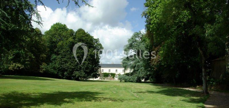 Vue d'une grande maison blanche entourée d'arbres, avec une pelouse verdoyante au premier plan.