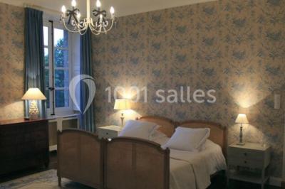 Chambre lumineuse avec un lit double, des rideaux fleuris, un lustre, des meubles classiques et des fenêtres donnant sur la…