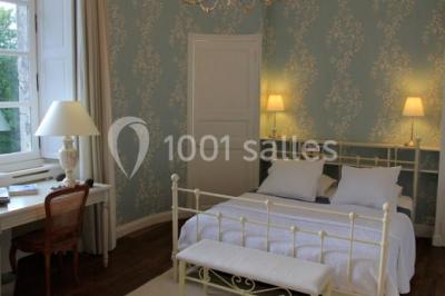 Chambre lumineuse avec un lit double, des rideaux fleuris, un lustre, des meubles classiques et des fenêtres donnant sur la…