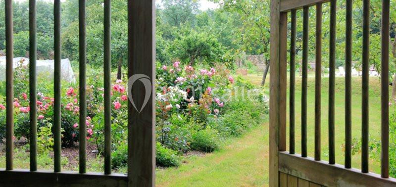Vue d'un jardin fleuri avec des rosiers et des arbres, encadrée par une porte en bois ouverte.